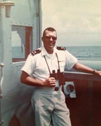 Image of young Neil Eney in naval uniform holding binoculars on a ship deck